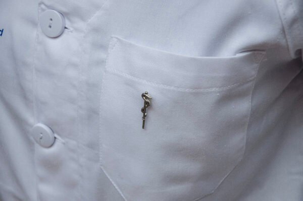 MedArtz Rod of Asclepius Pin displayed on the pocket of a white lab coat, lateral.