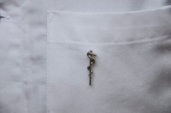 MedArtz Rod of Asclepius Pin displayed on the pocket of a white lab coat, front.