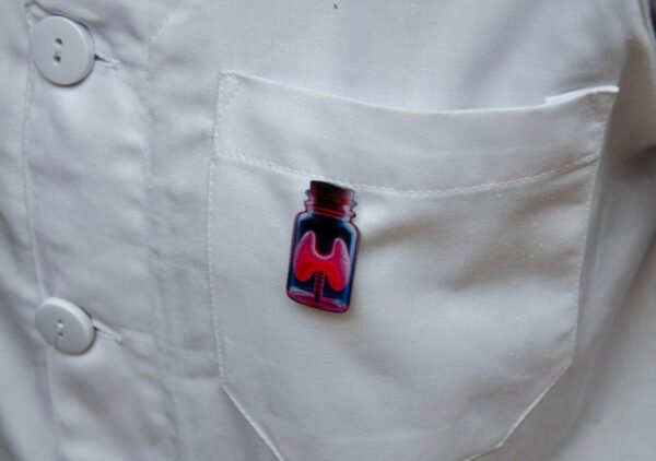 MedArtz Thyroid XL Pin on a white coat, lateral close view.